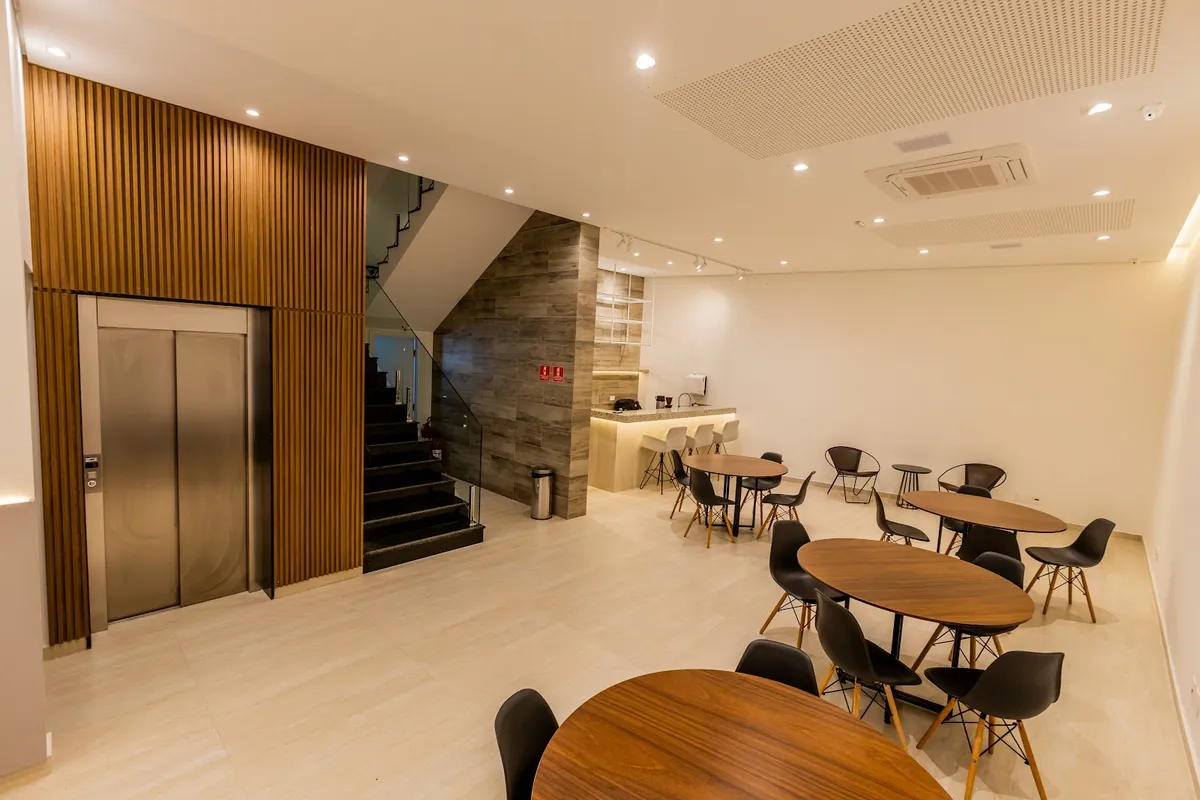 Térreo da Casa Versatt — lobby com elevador, escada e balcão de coffee